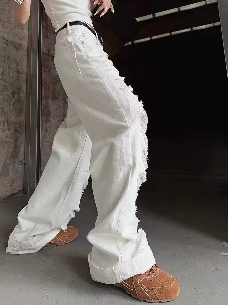 Person wearing white distressed jeans and brown shoes in a dark indoor setting.